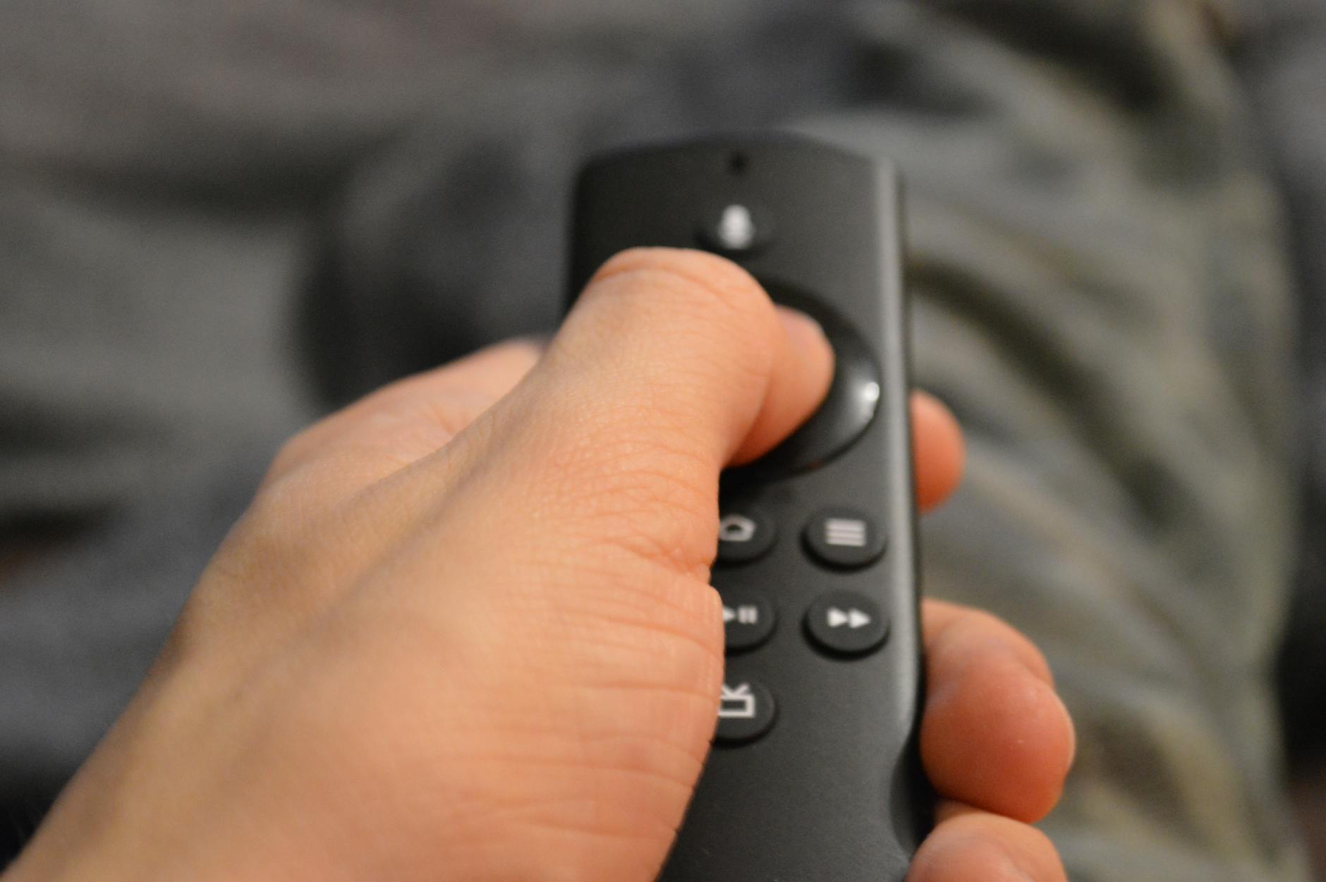 Hand holding TV remote control with streaming service buttons visible