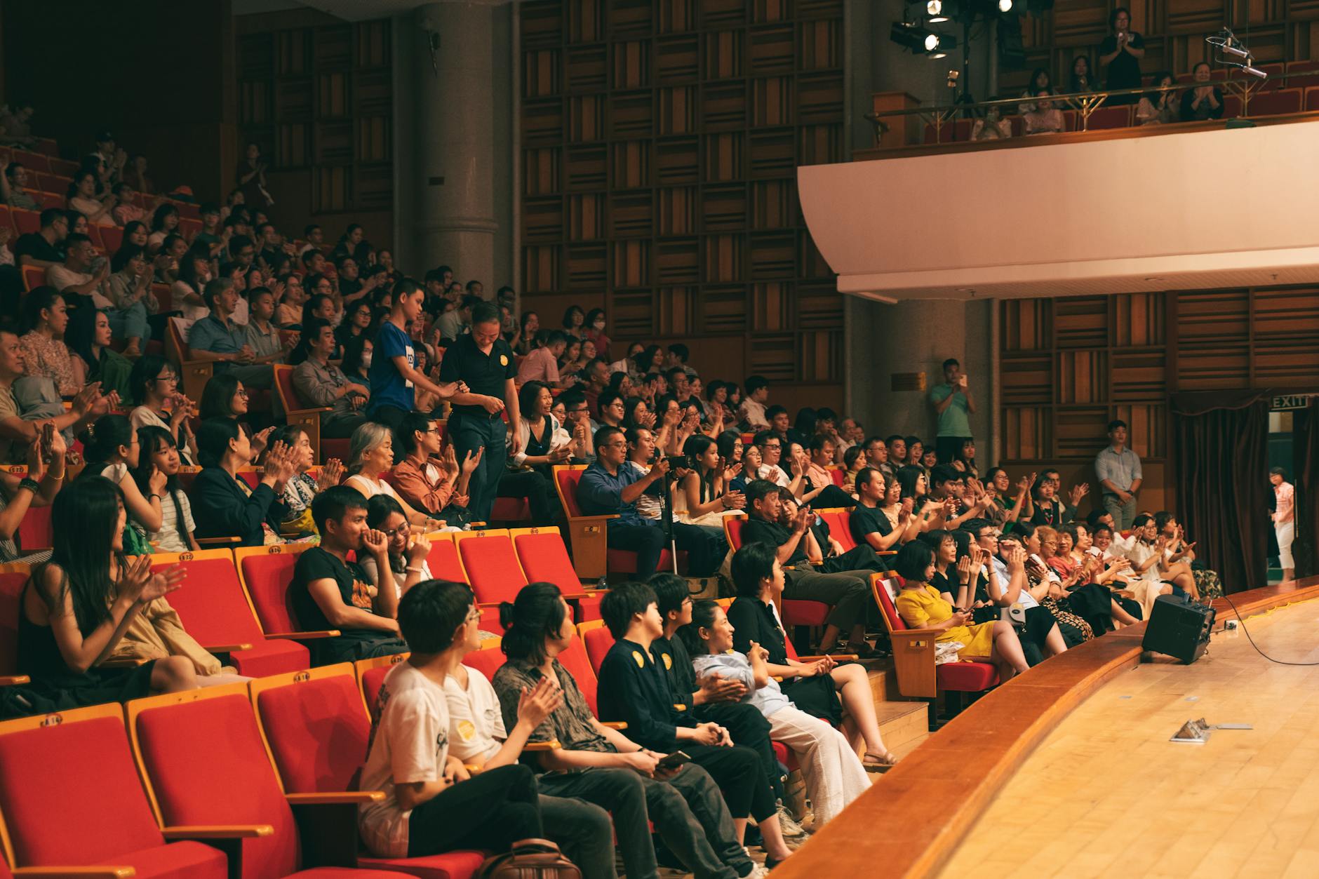 Theater audience members clapping and enjoying live performance in packed auditorium