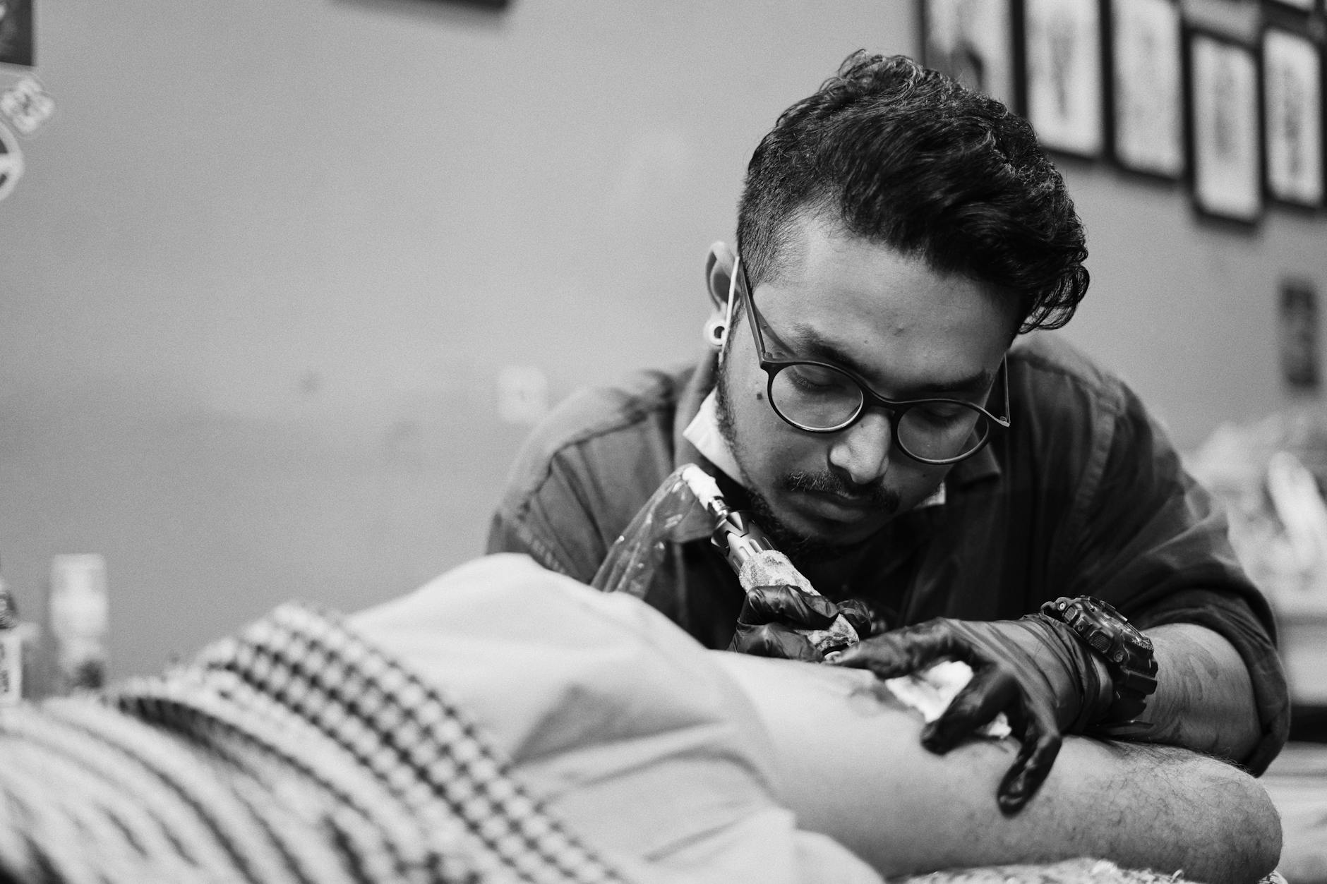 Tattoo artist concentrating on detailed work on a client's arm