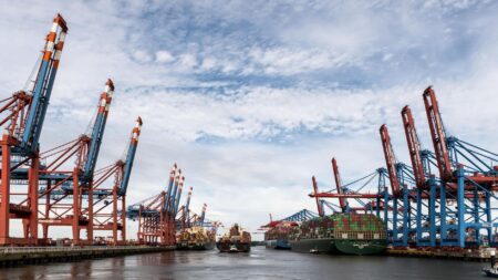 Large cargo containers stacked at an industrial shipping port, representing global commodity trade flows