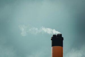 Carbon Credit Futures Quietly Draw Long-Only Allocators as Offsets Tighten Industrial smokestacks emitting carbon emissions into a grey sky, representing compliance carbon markets